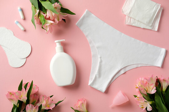 Top view feminine hygiene product on pink background. Flat lay composition with feminine pants, tampons, pads, menstrual cups, and a bottle of lotion on a pink background with flowers