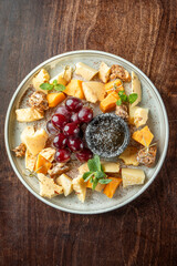 A visually appealing cheese platter featuring various cheese types, fresh grapes, and a small bowl of dark dip, garnished with mint leaves for added freshness.
