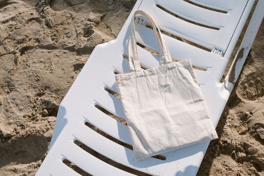White linen tote cotton, mesh bag on beach chair, sand background. Zero waste, no plastic, eco friendly shopping, recycling concept. Blank mockup shopper, place for art logo text. Flat lay copy space.
