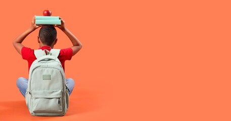 Little schoolboy with backpack holding books and apple on orange background, back view. Banner for...