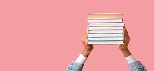Hands holding books on pink background with space for text