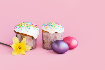Traditional russian Easter ortodox cake with daffodil flower and colorful eggs on light pink background. Kulic, Kulich, Paska homemade bread with glaze. Spring christian holiday. Festive celebration