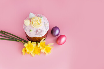 Traditional russian Easter ortodox cake with daffodil flower and colorful eggs on light pink background. Kulic, Kulich, Paska homemade bread with glaze. Spring christian holiday. Festive celebration