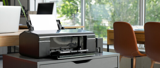 Modern printer on chest of drawers near desk in office