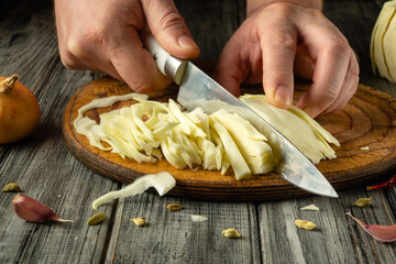 Hands skillfully slice fresh cabbage on a wooden cutting board surrounded by onions, garlic, and spices, capturing the essence of home cooking and preparation time