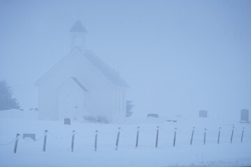 Small church and cemetery disappearing in the fog on a snowy winter day