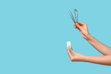 Female hands with dental tools and tooth model on blue background