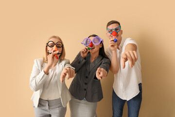 Business people in funny disguise with party whistles pointing at viewer on beige background. April...
