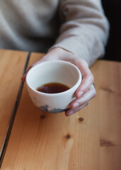 Young caucasian freelancer woman hold white cup with black filter coffee. Barista on cafeteria giving mug to customer top view. alternative brewing of specialty coffee, v60. background light wood