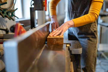 Woman carpenter hands operating electric planer, preparing and cutting wooden beams for future furniture. Woodshop production and craftswomanship, female work with precision and dedication to woodwork