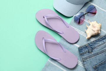 Flip flops with cap, sunglasses, blanket and jeans on turquoise background