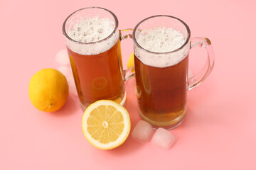 Glasses of fresh beer with lemon and ice cubes on pink background