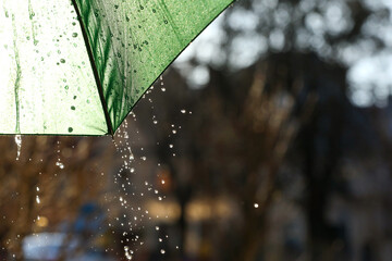 Open green umbrella under pouring rain outdoors, closeup. Space for text