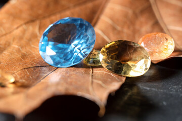 Beautiful shiny gemstones and dry leaf on black background, closeup