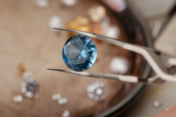 Tweezers with beautiful gemstone on blurred background, closeup