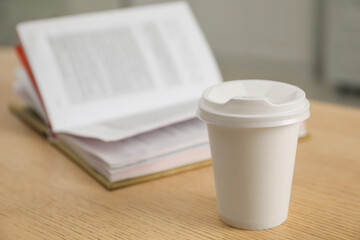 Paper cup and open book on wooden table indoors, closeup. Mockup for design