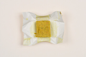 A top-down view of a bouillon cube in its opened wrapper on a light background