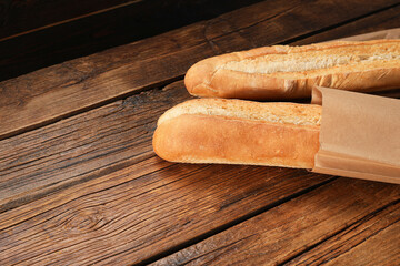 Paper bag with fresh baguettes on wooden table, space for text