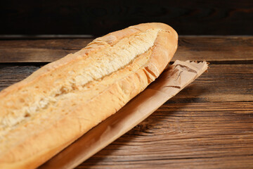 Paper bag and fresh baguette on wooden table, closeup. Space for text