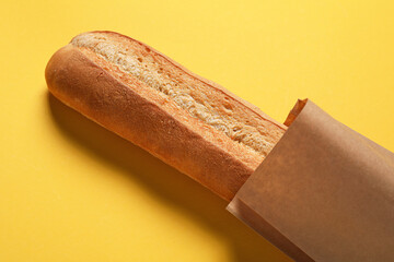 Paper bag with fresh baguette on yellow background, closeup