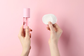 Woman with micellar water and clean cotton pads on light pink background, closeup