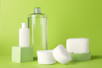Clean cotton pads and cosmetic products on green background. Space for text