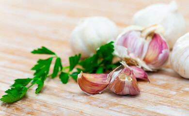 Fresh parsley stems and garlic cloves on wooden table.