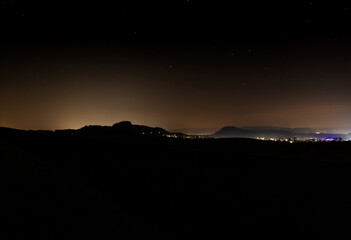 Nighttime landscape showcasing distant mountains and illuminated city skyline under a clear sky