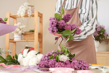Female florist making beautiful bouquet with lilacs in flower shop