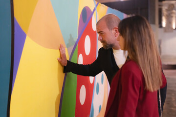 Art curator showing colorful modern painting to potential buyer