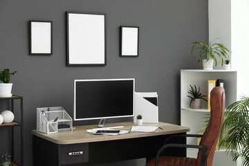 Workplace, modern computer, houseplant and pictures near black wall in office