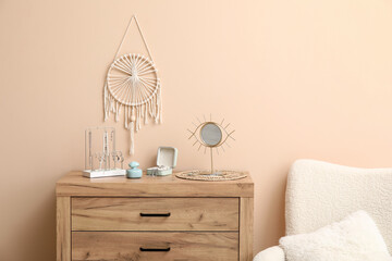 Organizers with stylish different jewelry, mirror and perfume bottle on dresser near beige wall
