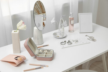 Organizers with stylish different jewelry, mirror and photo frame on table near window