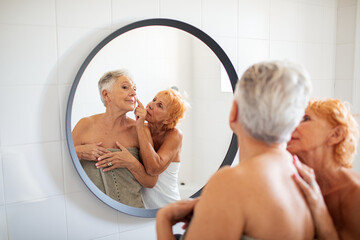 Senior lesbian couple looking at mirror in bathroom after shower