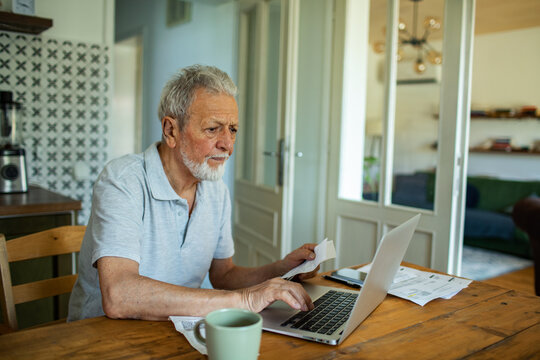 Senior man managing finances online with laptop at home - Powered by Adobe