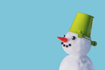 View of the snowman in a hat in the form of a bucket on a blue isolated background. Holiday...