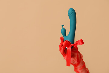 Woman in laced glove holding vibrator with bow on color background, closeup