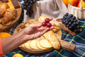 Close-up view of a picnic with food laid out and hands holding food, selective focus. The concept of summer outdoor recreation on the weekend