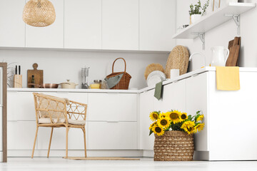 Interior of light kitchen with armchair, counters and sunflowers in basket