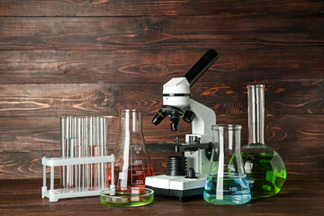 Modern microscope with chemical flasks on table against wooden background