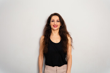 Naklejka premium Positive relaxing make-up woman with red lipstick, long brown hair looking happy in black summer top on blue studio empty copy space background. Expression front view portrait