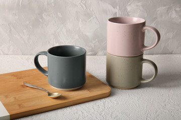 Composition with ceramic mugs, wooden tray and teaspoon on white table near grey wall