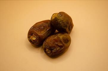 Close-up of three dried ramadan dates on a beige background, showcasing their wrinkled texture and rich brown color