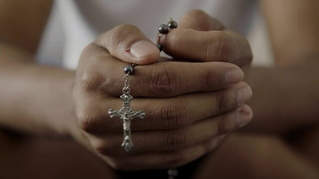 Hands holding rosary beads while praying