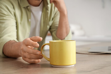 Young man taking ceramic cup from table in kitchen, closeup