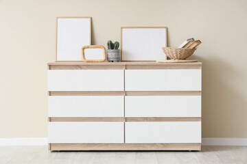 Chest of drawers with frames and decor near beige wall in room © Pixel-Shot