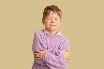 Smiling little boy in warm sweater hugging himself on green background
