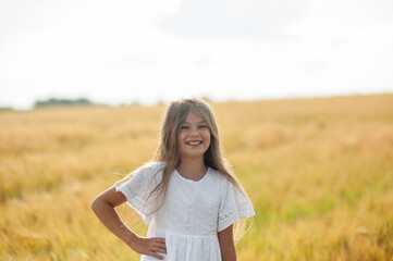 Little happy girl in white dress running on sunny wheat field