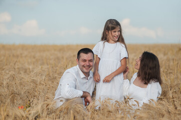 Mom, dad and  сute daughters hug in a wheat field.