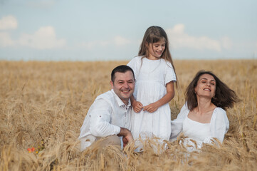 Mom, dad and  сute daughters hug in a wheat field.